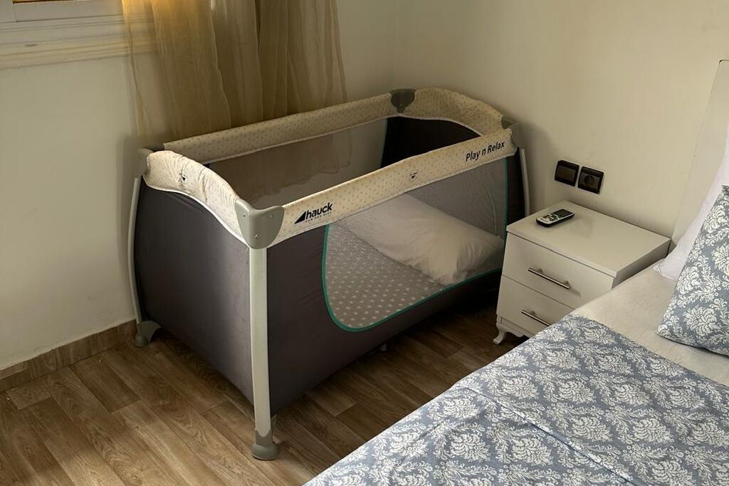 Un berceau pour bébé avec un tapis de jeu, une table de chevet avec une lampe et une couverture de lit à motifs.