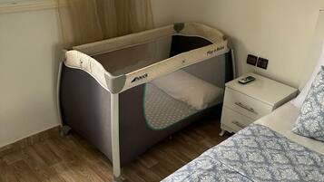 Un berceau pour bébé avec un tapis de jeu, une table de chevet avec une lampe et une couverture de lit à motifs.