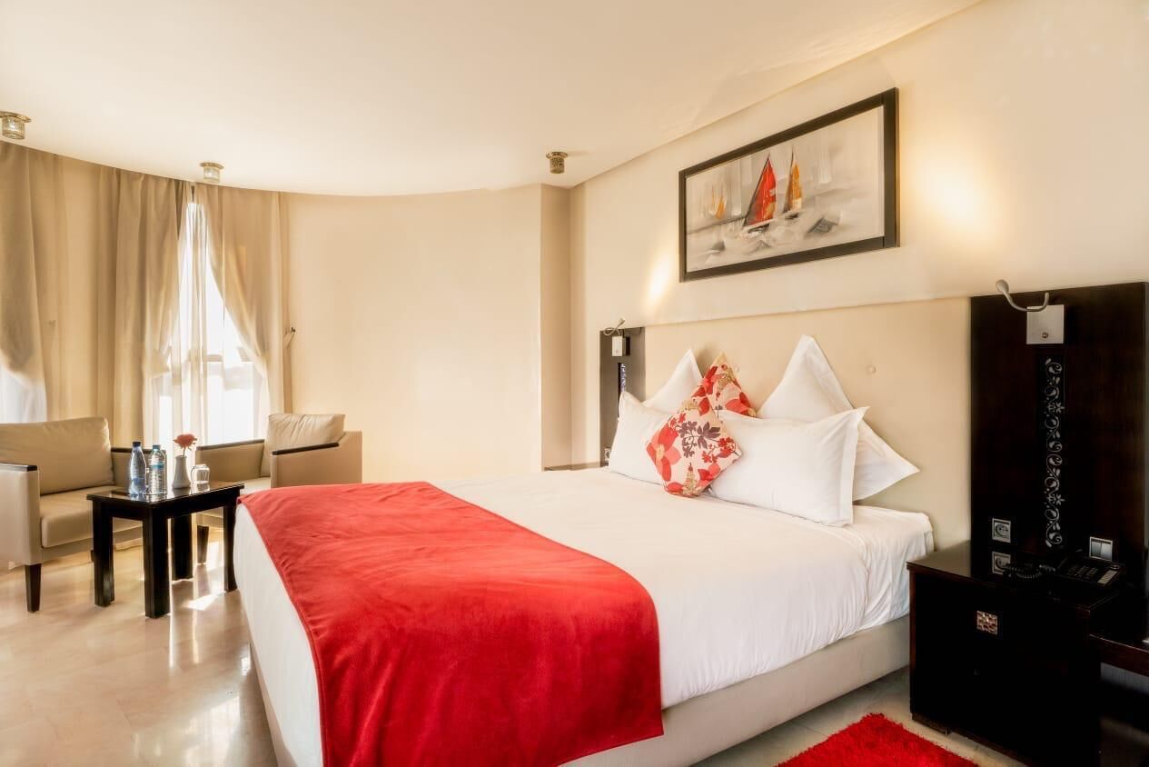 A hotel room with a bed, a desk, a chair, a nightstand, and a painting on the wall.
