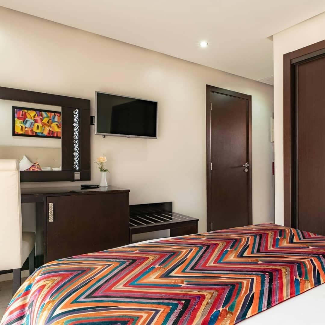 Ein Hotelzimmer mit einem Bett, einem an der Wand montierten Fernseher, einem Schminktisch und einer Tür.