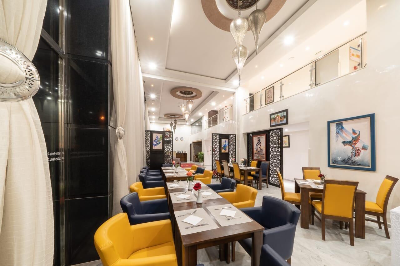 A hotel dining area with multiple tables and chairs, a chandelier, and artwork on the walls.