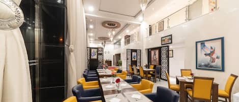 A hotel dining area with multiple tables and chairs, a chandelier, and artwork on the walls.