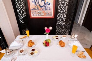 A breakfast table set with croissants, fruits, and beverages, with a decorative vase of flowers in the center.