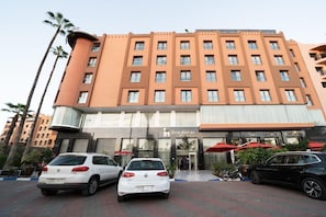 A multi-story hotel with a modern facade, featuring a prominent entrance with glass doors and red umbrellas.