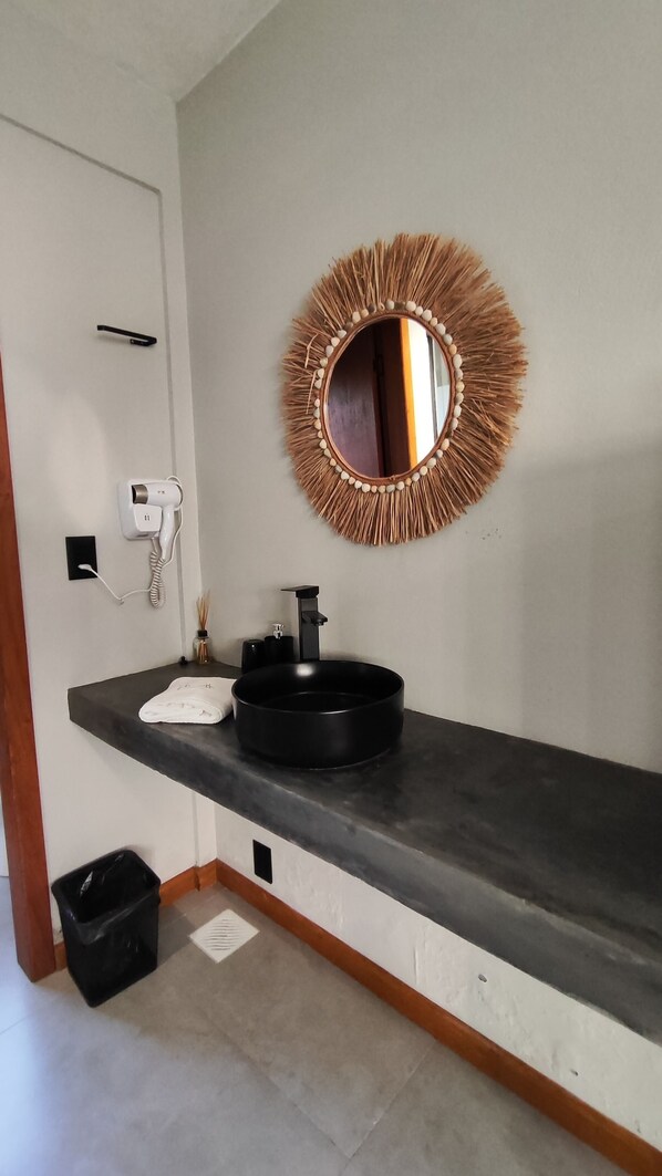 A bathroom with a round mirror, black sink, and a hairdryer on the wall.