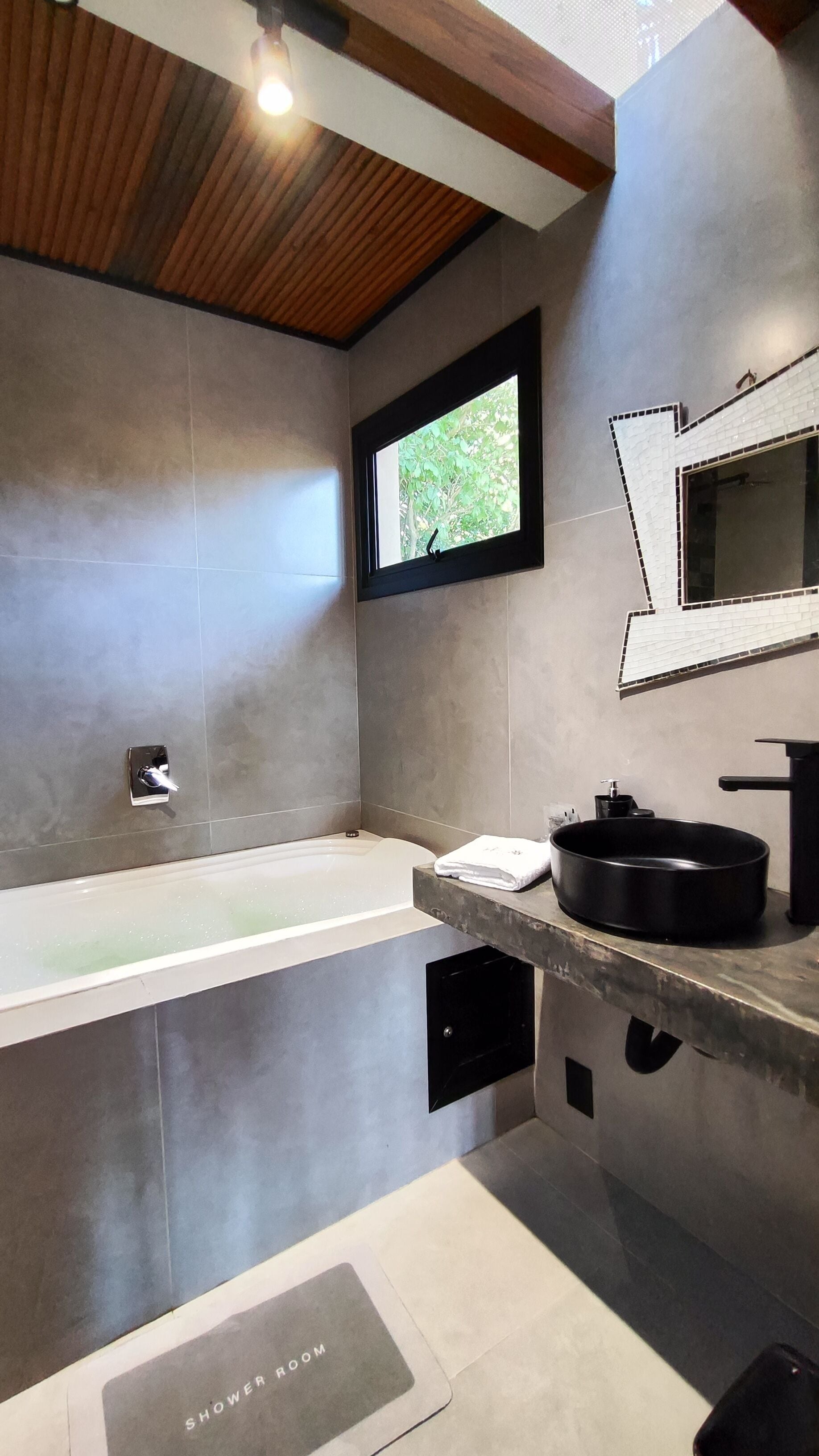 A modern bathroom with a bathtub, a sink with a black basin, and a window with a view of greenery.