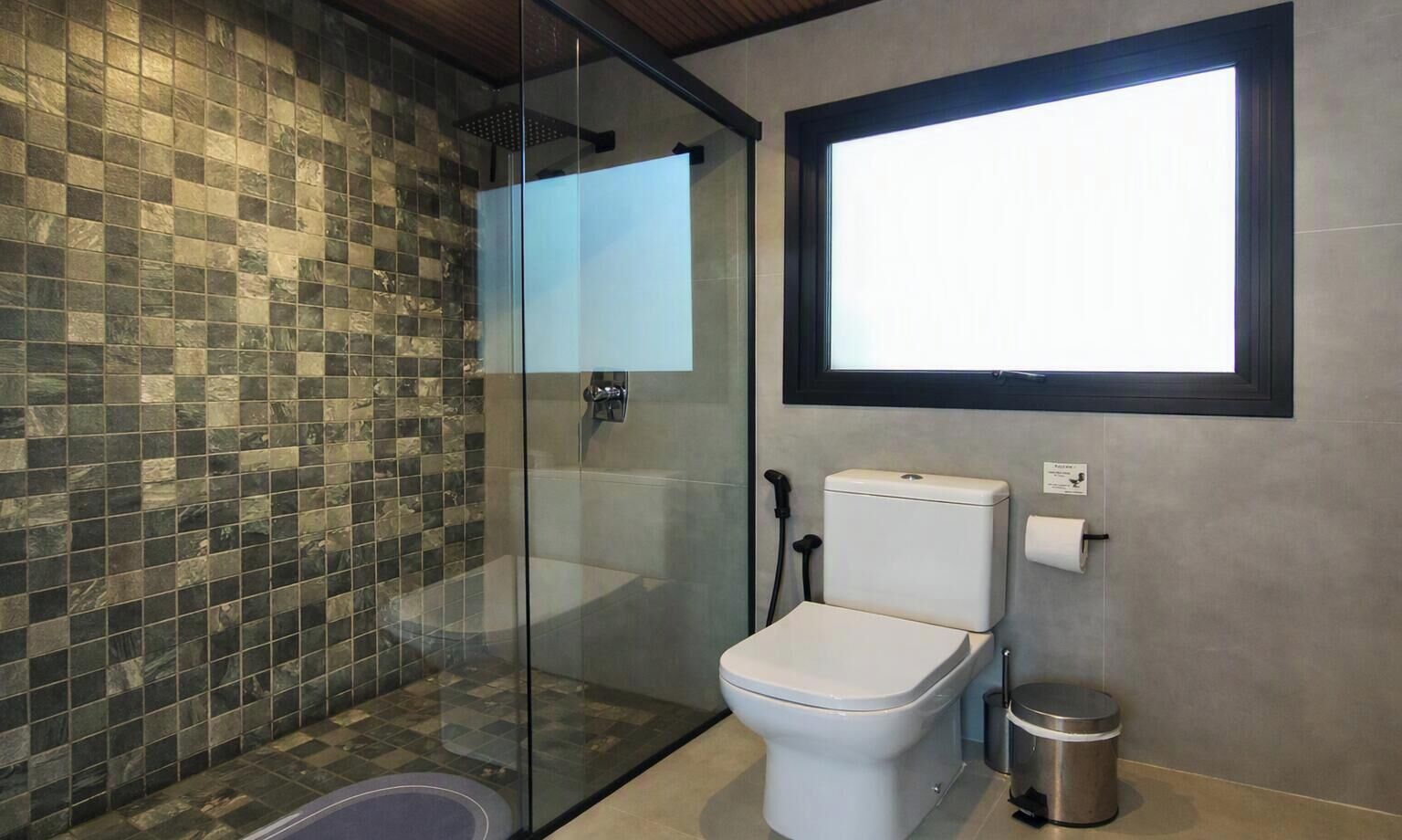A bathroom with a glass-enclosed shower, a toilet, and a window.