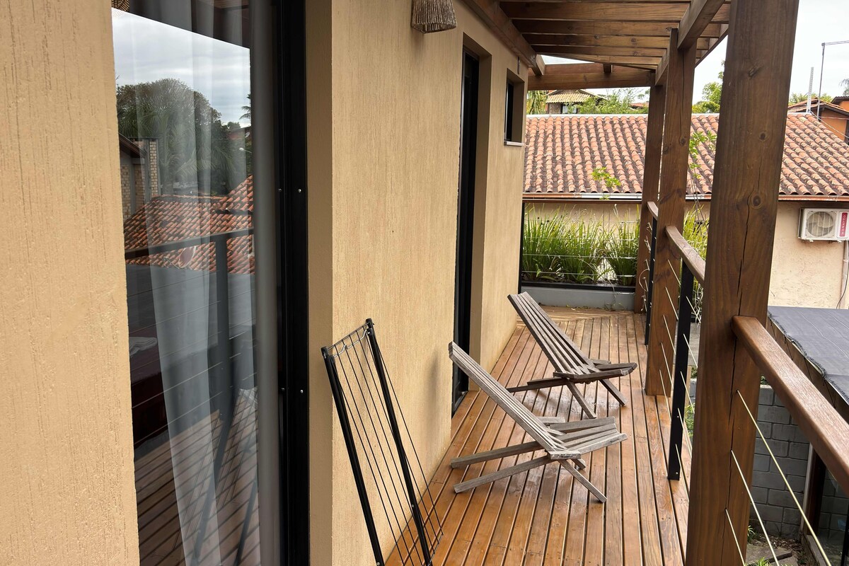 A wooden deck with two lounge chairs and a glass door leading to a balcony.