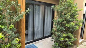 A modern building with a sliding glass door, a wooden fence, and various green plants.