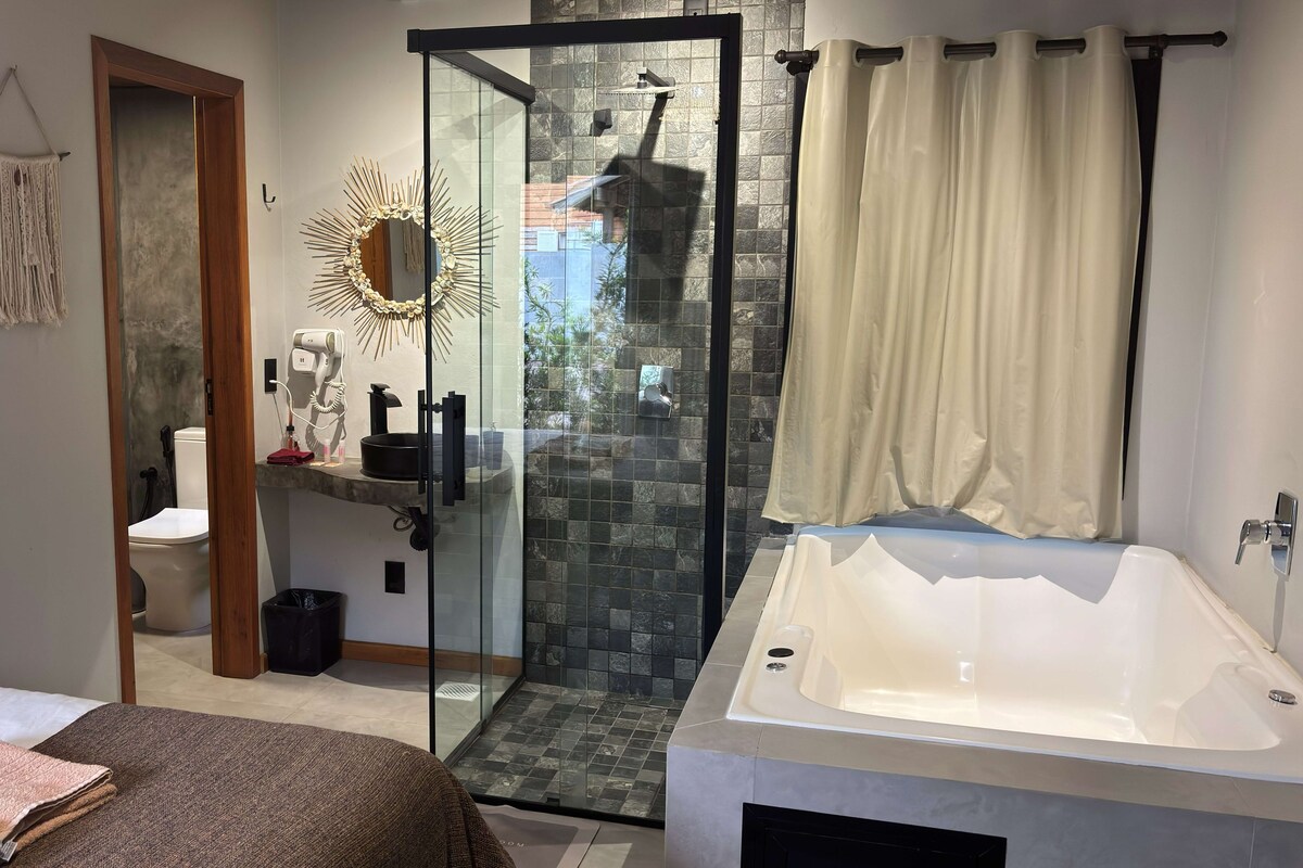 A modern bathroom with a glass-enclosed shower, a large bathtub, and a toilet visible through a doorway.
