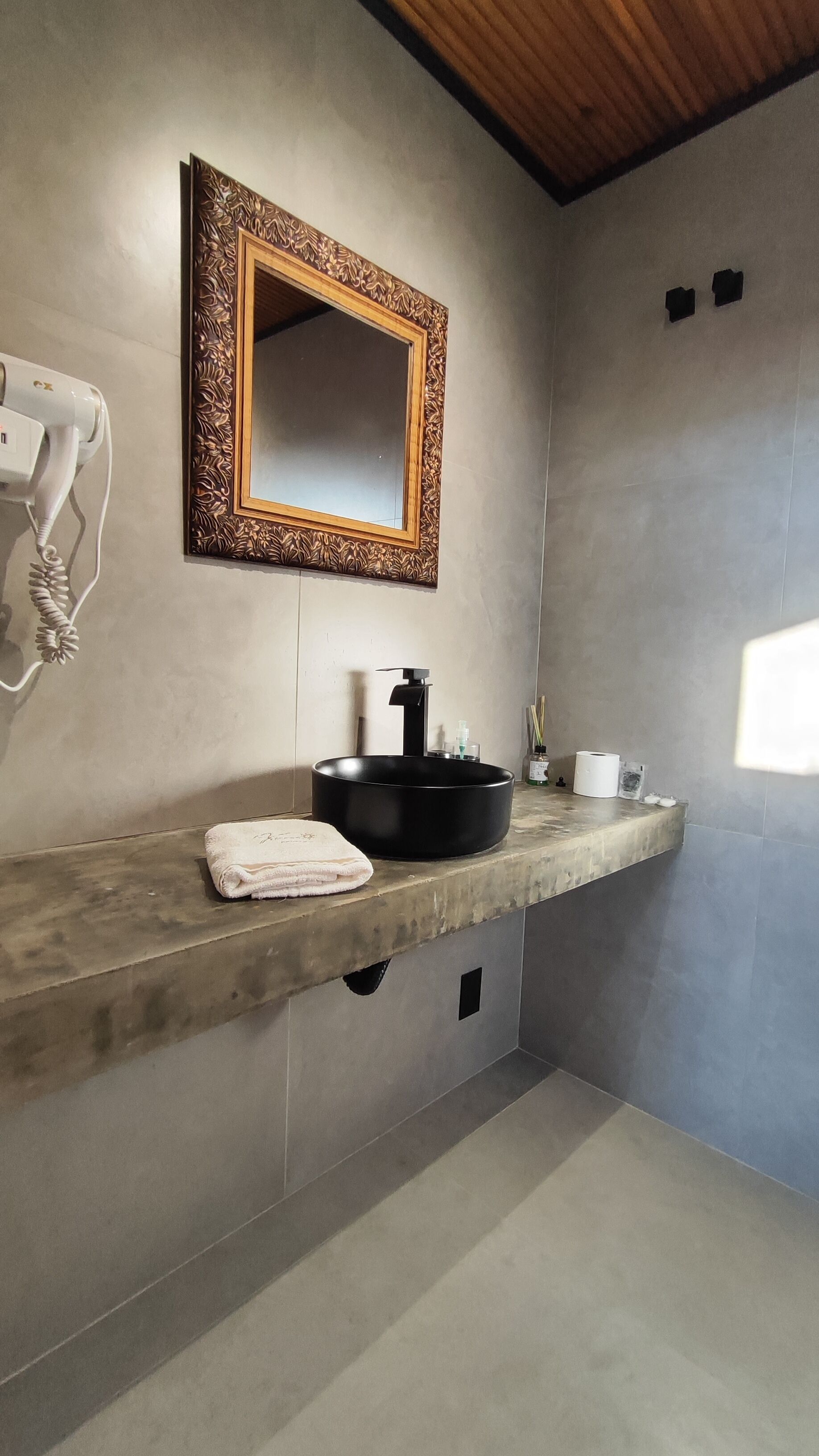 Un baño con un espejo grande, un lavabo negro, una toalla y un secador de pelo.
