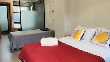 Una habitación de hotel con una cama grande, una cama más pequeña, una colcha roja, una lámpara colgante y un aire acondicionado instalado en la pared.
