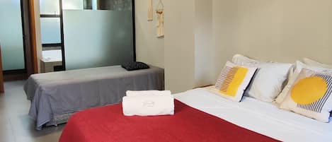 A hotel room with a large bed, a smaller bed, a red blanket, a hanging light fixture, and a wall-mounted air conditioner.