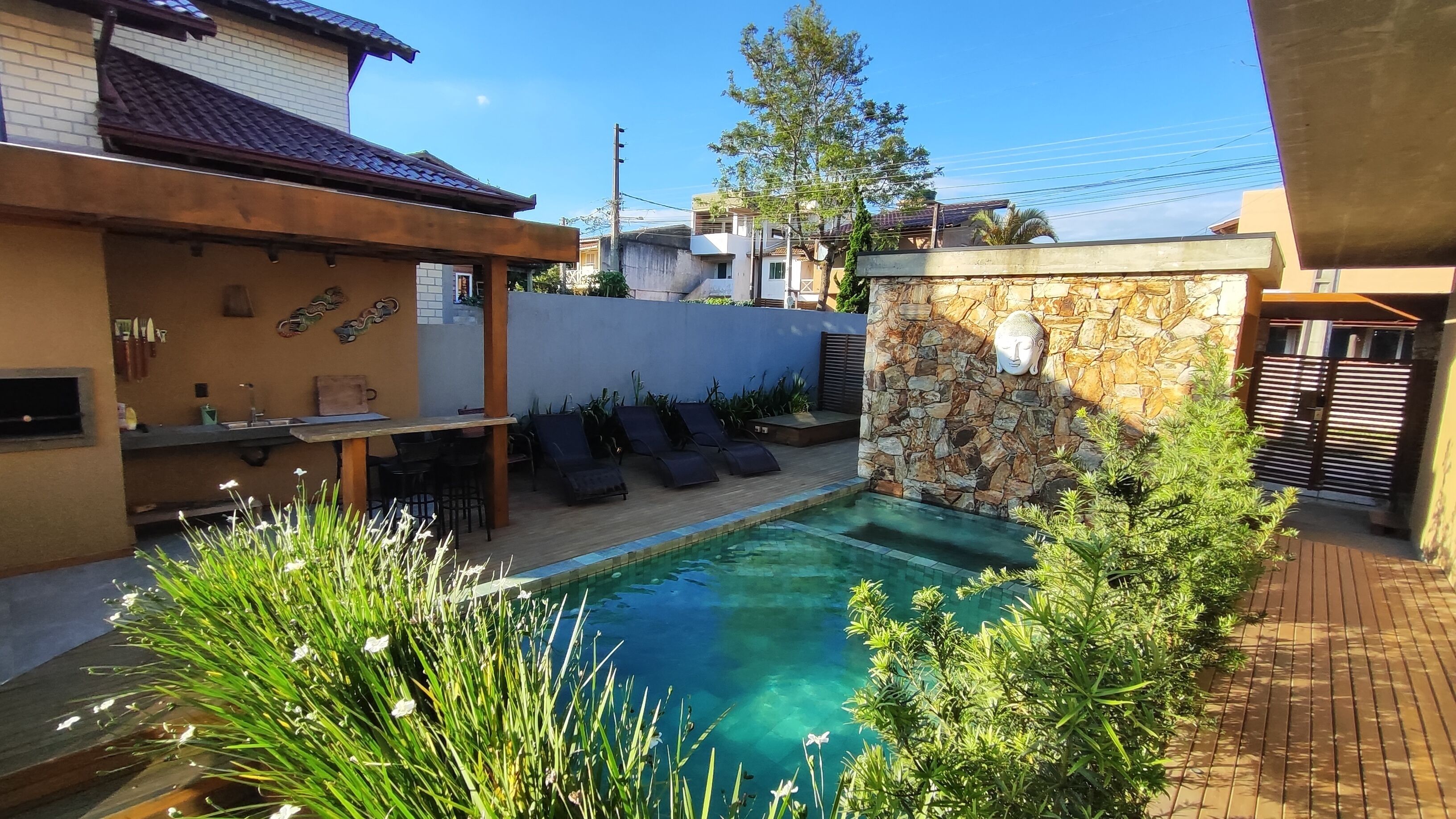 Una piscina con sillas de descanso, un muro de piedra y una escultura de cabeza de Buda.