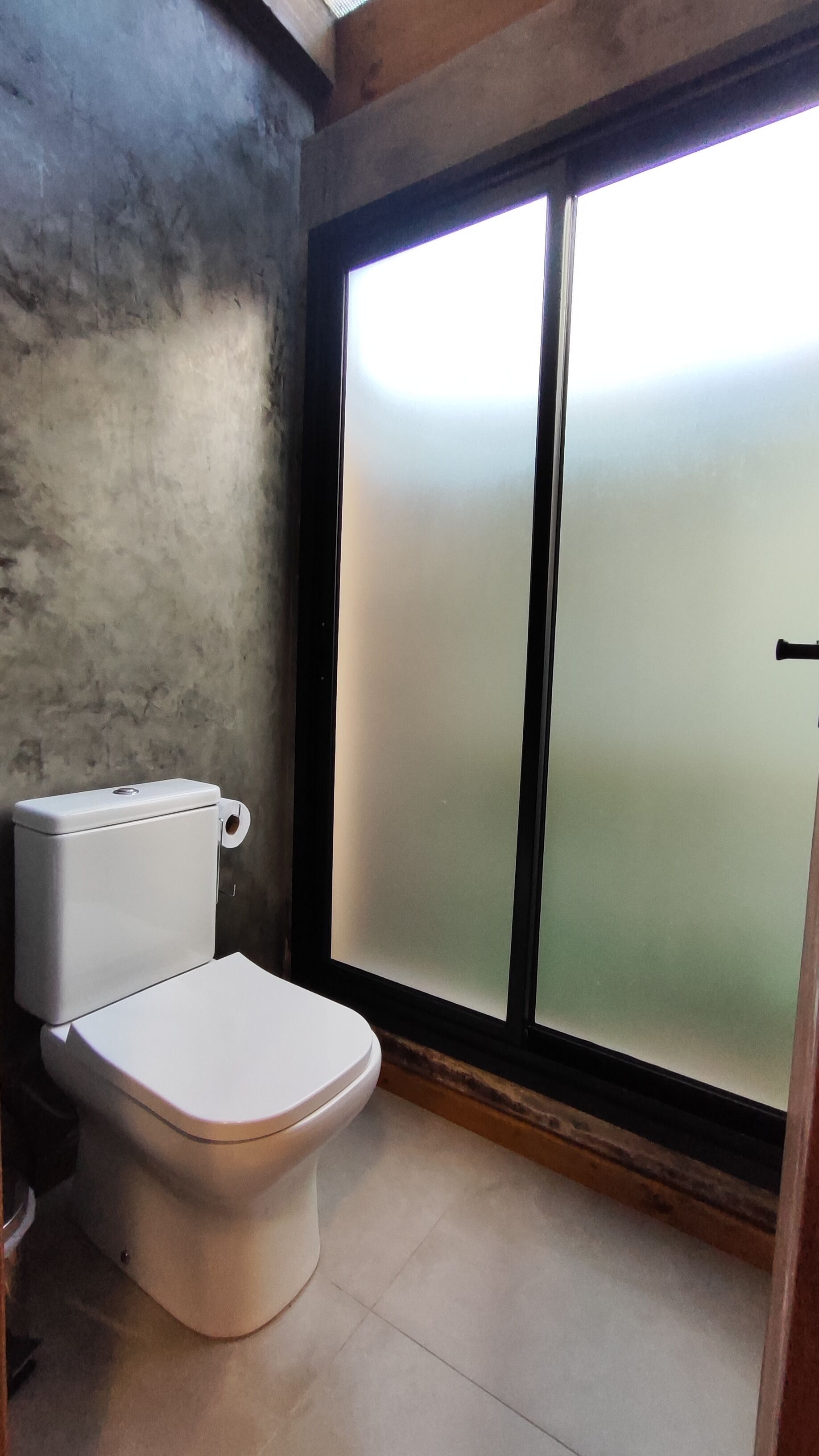 A bathroom with a toilet, a window with frosted glass, and a tiled floor.