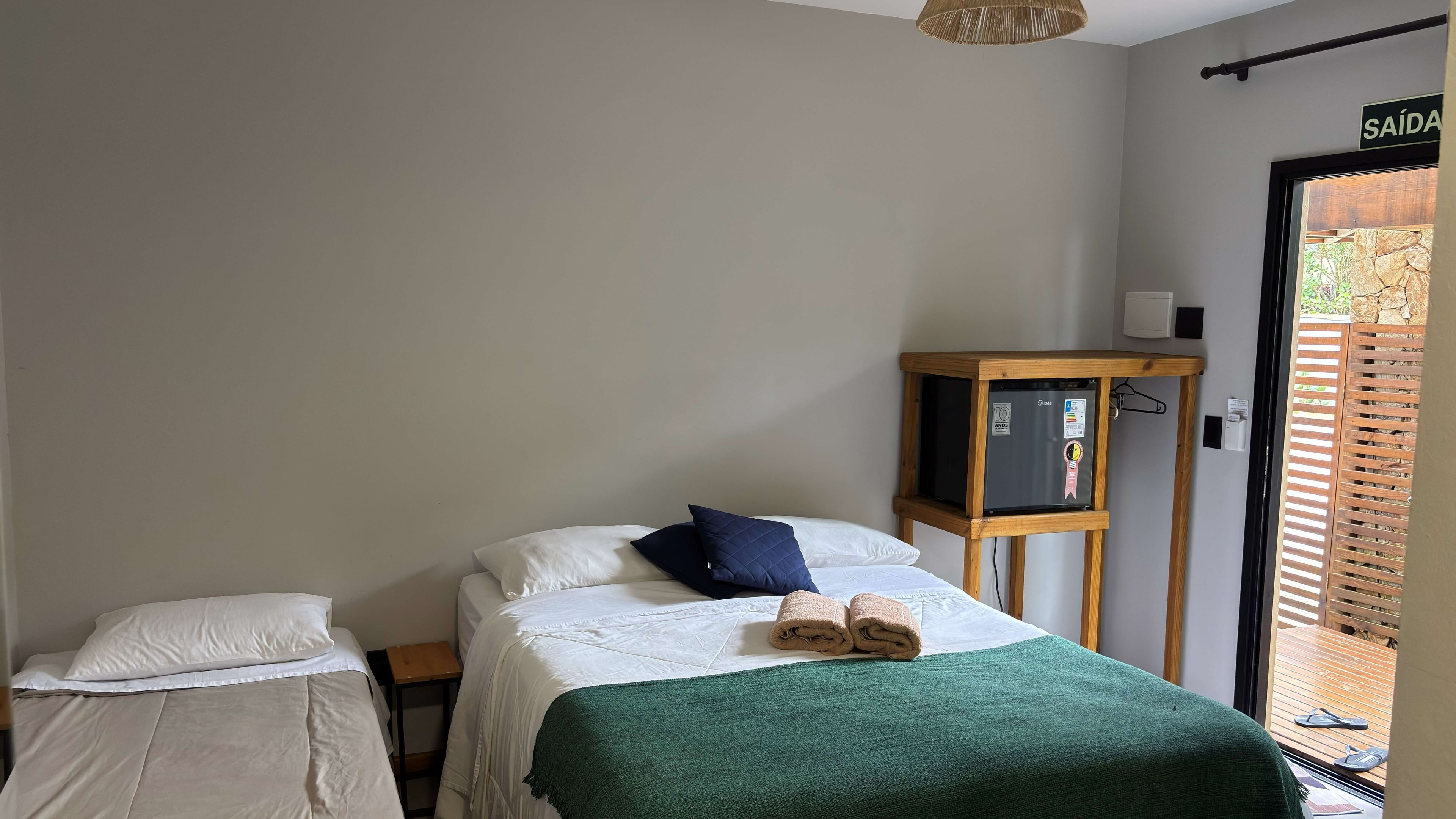 Un dormitorio con dos camas, un pequeño armario de madera, una manta verde y una puerta que da al exterior.