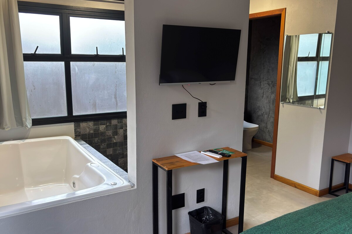 A bathroom with a bathtub, a toilet, a mirror, and a television mounted on the wall.