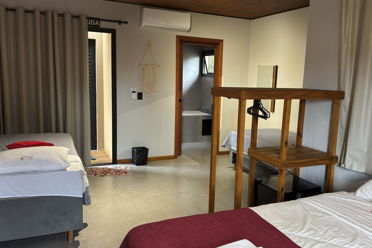 A hotel room with two beds, a wooden chair, a small table, a mirror, and a view of the bathroom.