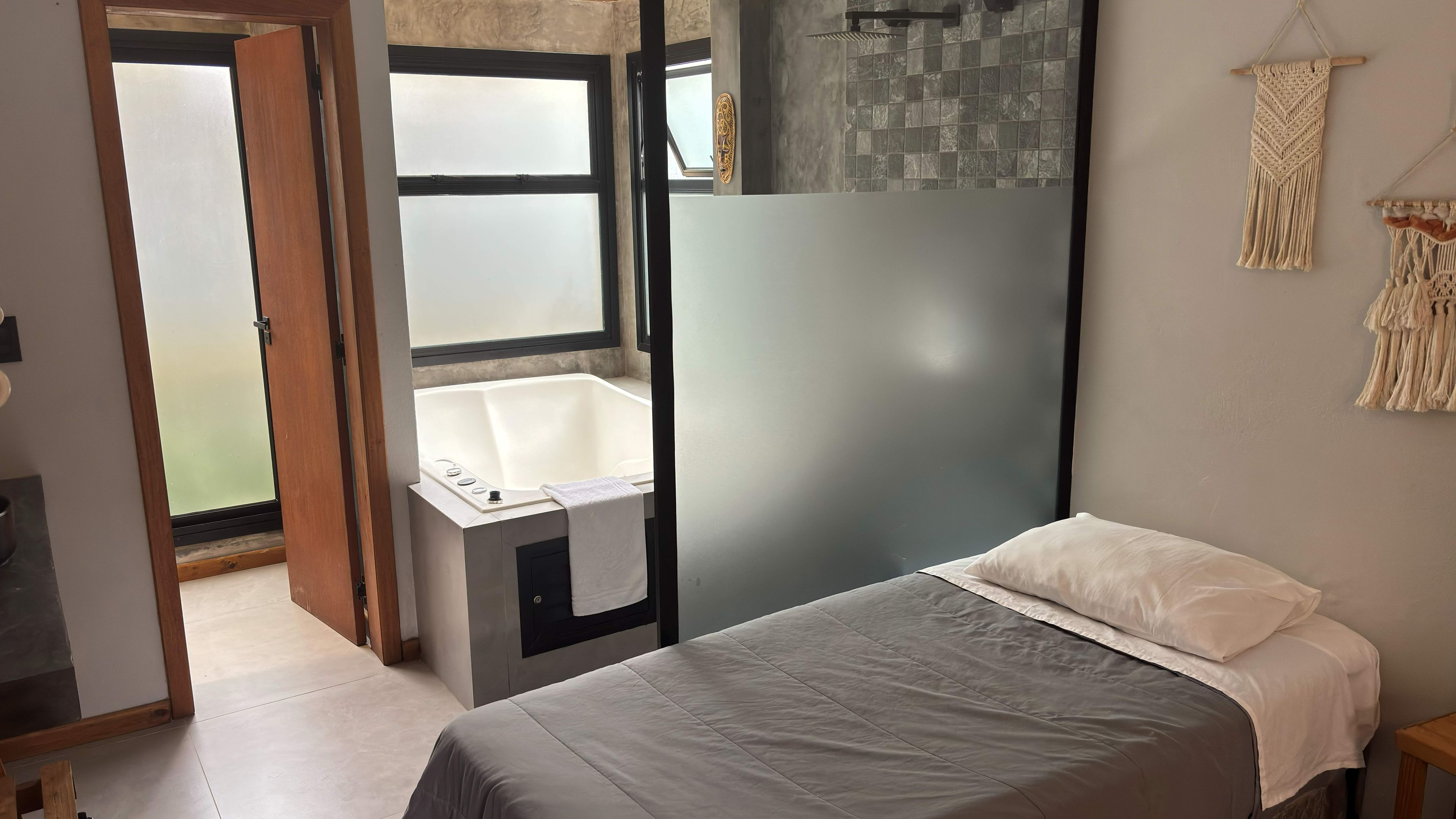 A bedroom with a bed, a small bathroom with a bathtub, and a view through an open door.