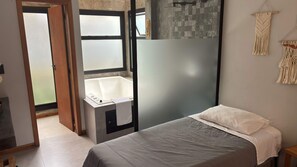 Un dormitorio con cama, un baño pequeño con bañera y vistas a través de un ventanal abierto.