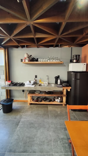 A kitchen with a gas stove, sink, and a black refrigerator. There are shelves above the counter holding various kitchen items.