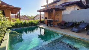 A swimming pool with a wooden deck, lounge chairs, and a bar area.