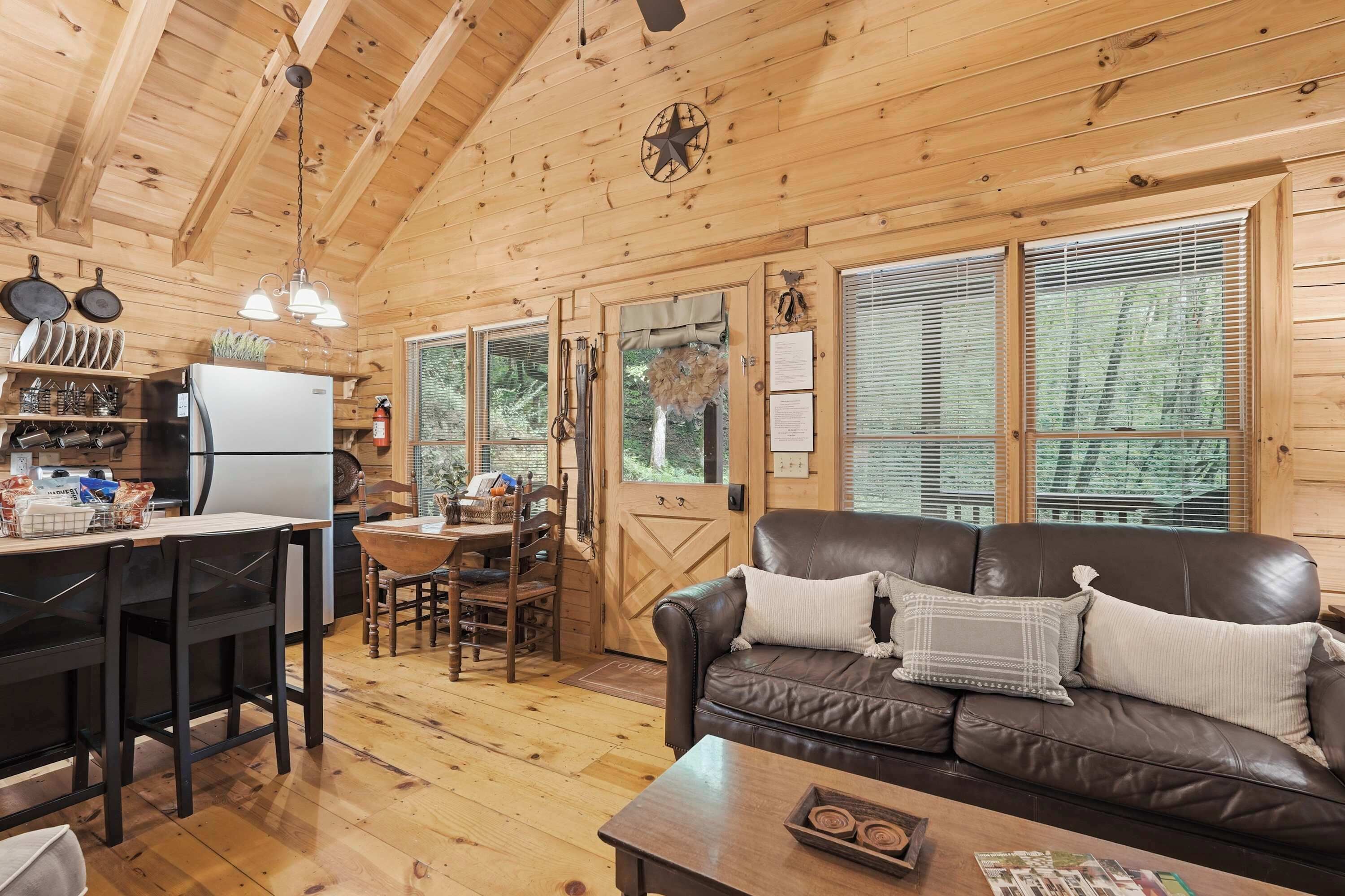 A cozy cabin interior with a dining area, a kitchen, and a living room with a leather couch.
