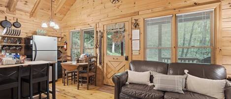 A cozy cabin interior with a dining area, a kitchen, and a living room with a leather couch.