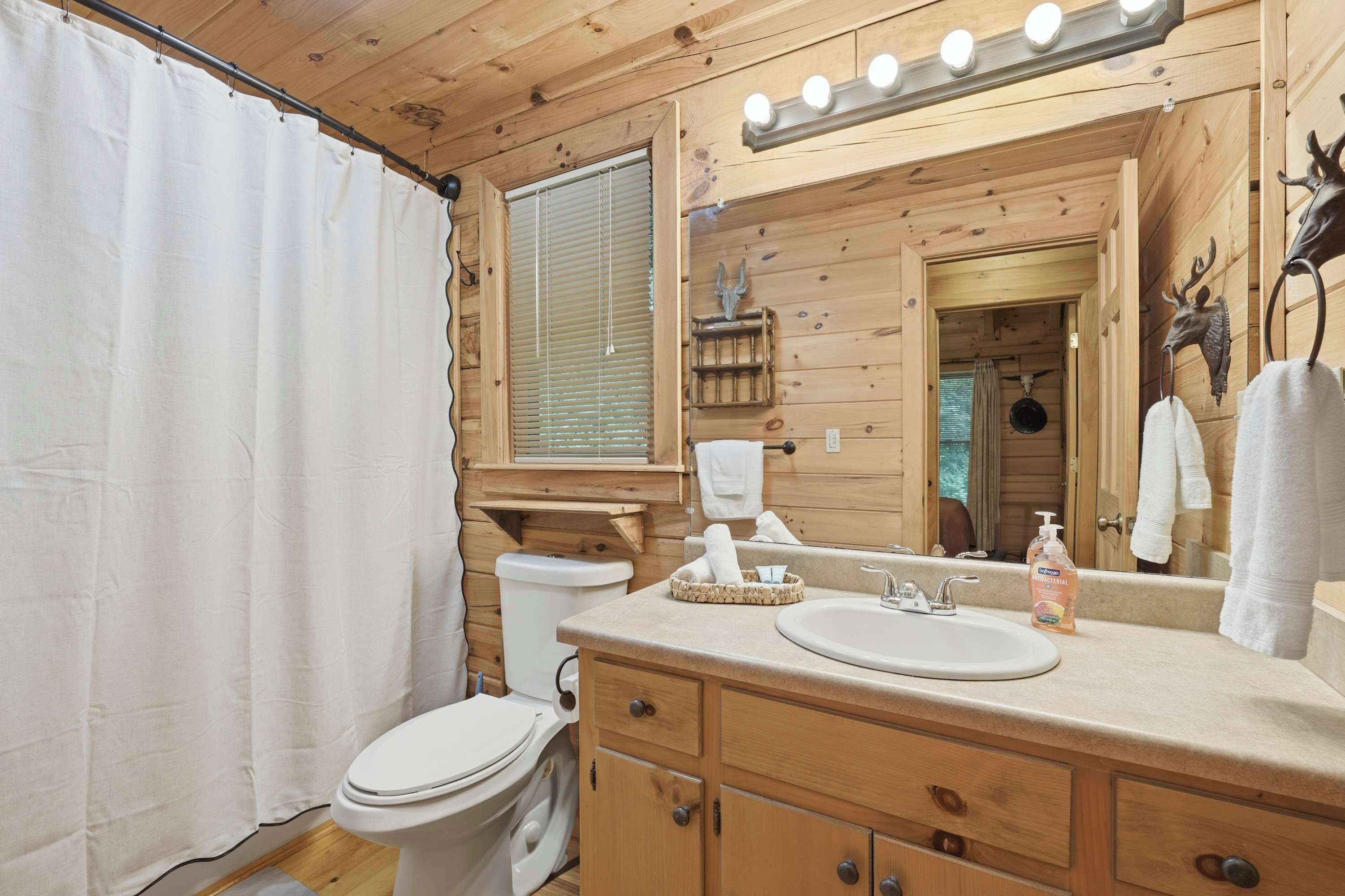 A wooden cabin bathroom with a toilet, sink, vanity, and a mirror with lights.