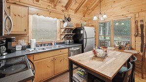 Una cucina in baita di legno con un'isola centrale, elettrodomestici in acciaio inossidabile e una finestra con persiane.