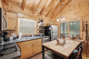 Eine Holzhütte mit einer Küche, einer zentralen Kochinsel, Edelstahlgeräten und einem Fenster mit Jalousien.