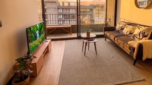 A modern living room with a flat-screen TV, a sofa, a small table, and a large window with a view of buildings. - Santiago Centro Histórico-Domus Travels (Santiago)