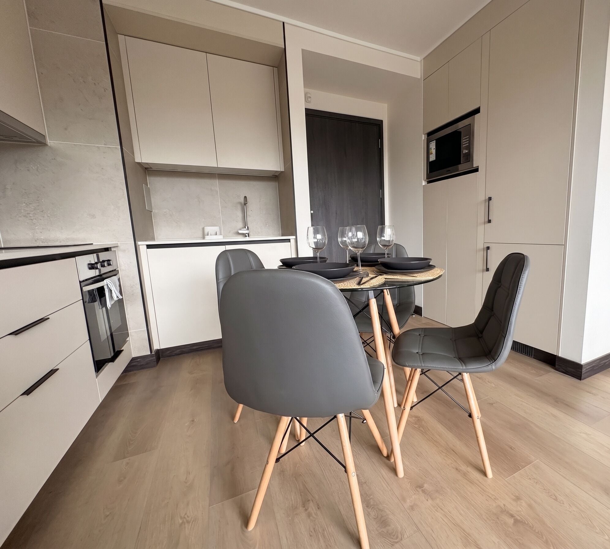 A modern kitchen with a dining area, featuring a table with chairs, a microwave, and a window.