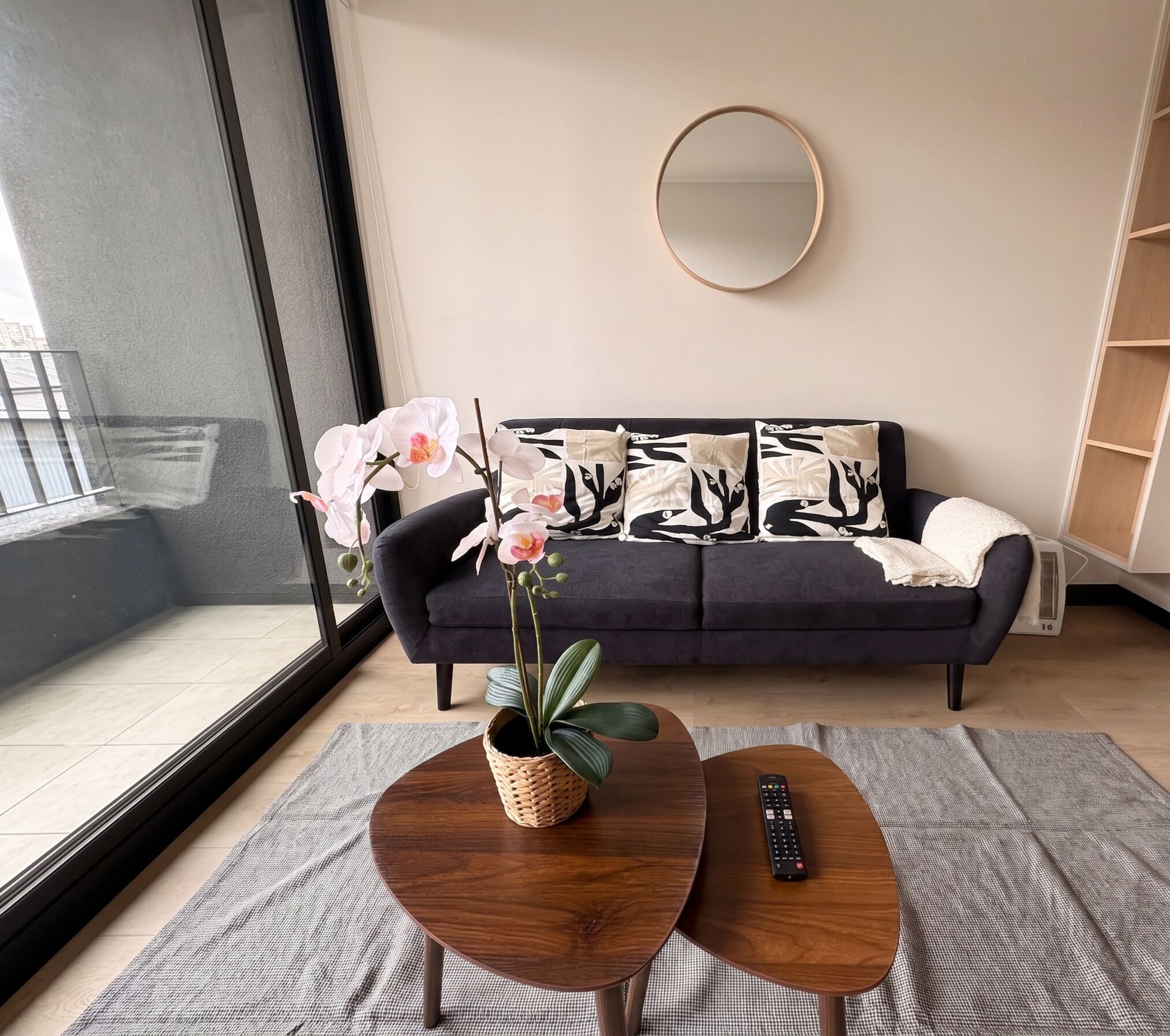 A modern living room with a dark sofa, a round mirror, and a coffee table with a remote control.