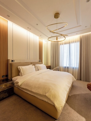 Quarto de hotel moderno com uma cama grande, cabeceira de madeira, roupeiro embutido e luminária circular no teto.