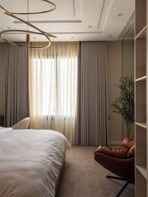 Une chambre moderne avec un grand lit, un fauteuil en cuir marron et une grande fenêtre avec des rideaux.