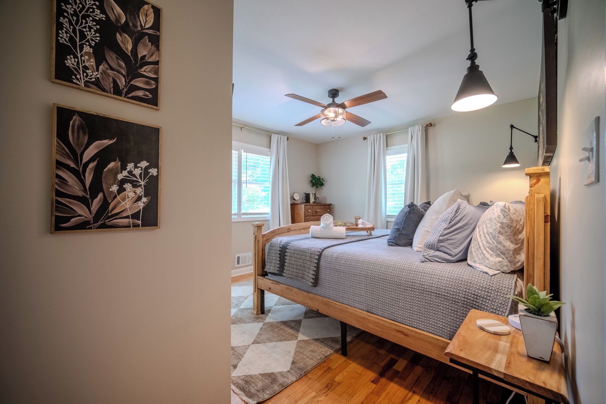A bedroom with a bed, a ceiling fan, a bedside table with a lamp, and a window with curtains.
