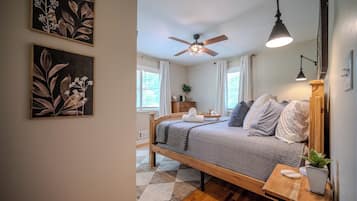 A bedroom with a bed, a ceiling fan, a bedside table with a lamp, and a window with curtains.