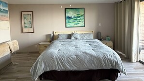 Et soveværelse med seng, loftventilator, natbord, lampe og et vindue med gardiner.