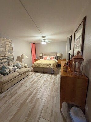 Et soveværelse med seng, sofa, loftventilator og et natbord med lampe.