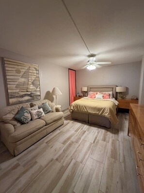 A bedroom with a bed, a sofa, a ceiling fan, and a painting on the wall. - Breathtaking Ocean View, 3 Cozy bedroom/2 bath Condo. Swimming pool/Tennis court (South Padre Island)