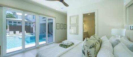 A hotel room with a large bed, a ceiling fan, a view of a swimming pool, and a door leading to a balcony.