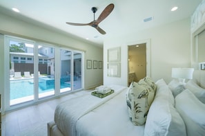 Ein Hotelzimmer mit einem großen Bett, einem Deckenventilator, Blick auf einen Swimmingpool und einer Tür zu einem Balkon.