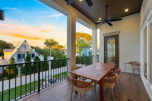 Ein Balkon mit Holztisch und Korbstühlen, mit Blick auf ein Wohngebiet mit Häusern und Bäumen.