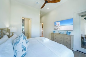 Ein Schlafzimmer mit einem Bett, einem Deckenventilator, einer Kommode und einem Fernseher, der eine Strandansicht zeigt.