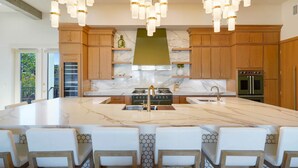 Une cuisine dotée d’un grand îlot central, de meubles en bois, d’une cuisinière en acier inoxydable et d’un luminaire suspendu au design moderne.