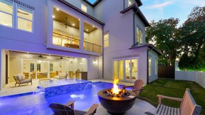 Une maison à deux étages dotée d’une piscine, d’un espace salon extérieur et d’un foyer.