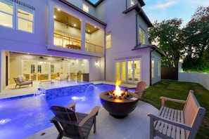 Ein zweistöckiges Haus mit Swimmingpool, Sitzgelegenheiten im Freien und einer Feuerstelle.