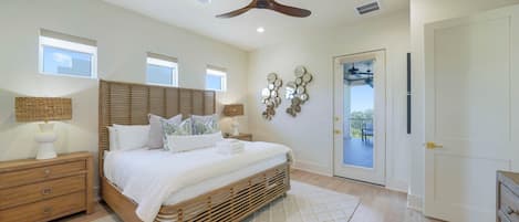Un dormitorio con cama, mesitas de noche, ventilador de techo y puerta que da a un balcón.