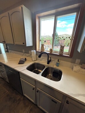 A kitchen with a double sink, a window with a view of the outdoors, and a countertop with various items. - Great 3 bedroom home for outdoor enthusiasts and families! (Mancos)